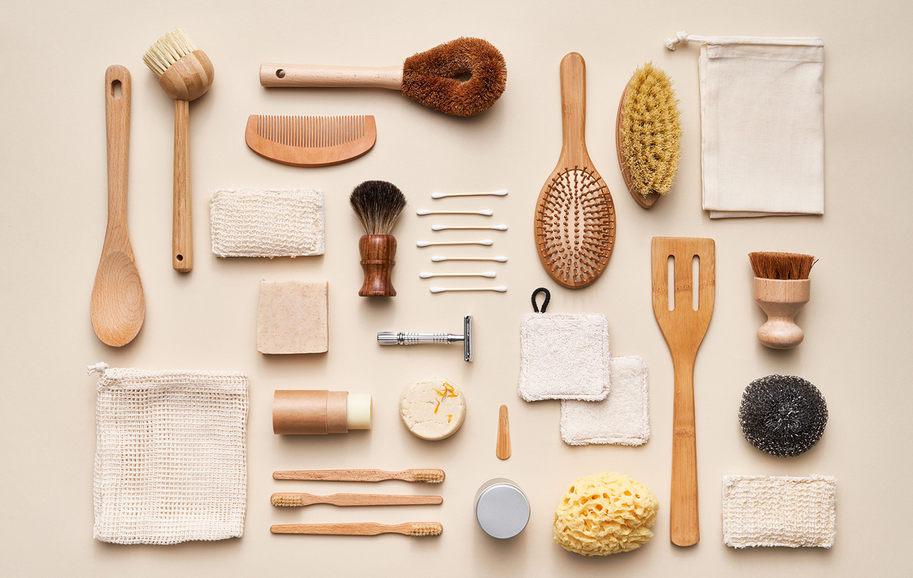 Overhead collection of various natural cosmetic products and bamboo reusable tools placed on beige background